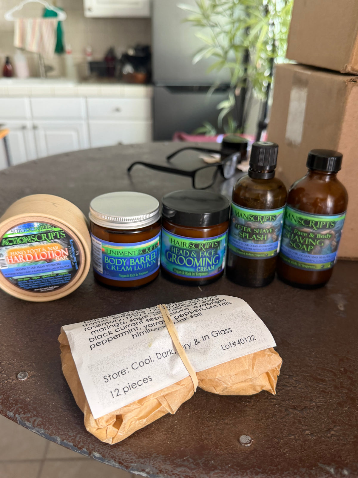 A collection of haircare products from Hair & Roots, including a Hard to Day body butter jar, grooming cream jar, and three amber bottles, alongside a wrapped bundle of brown paper towels on a dark tabletop.