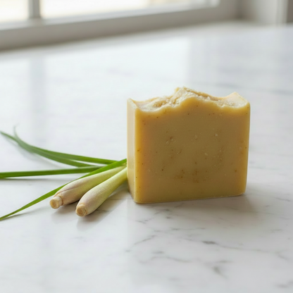 A rectangular bar of pale yellow soap with a rustic, hand-cranked top, styled with fresh green onions on a white marble countertop.
